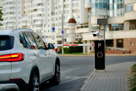 SUV stopped in front of closed automatic parking barrier gate with security surveillance camera. Automated parking control system, access terminal and stopped car. Parking access control terminal