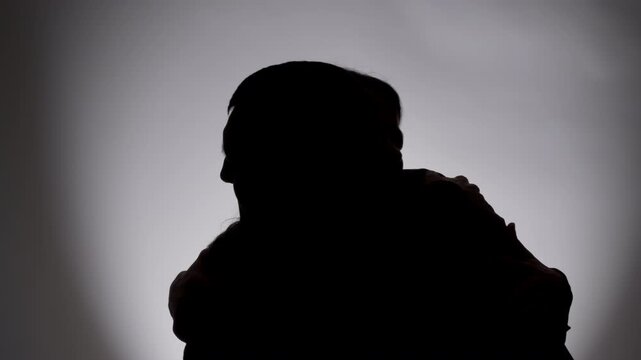 Silhouette of man and woman standing opposite each other before embrace. Side view portrait showing male female figures in backlit studio.
