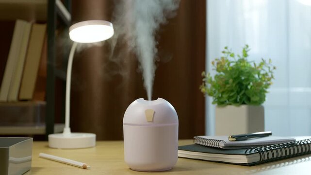 Modern ultrasonic air humidifier emitting mist on wooden desk in home office.