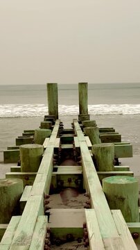 Wooden pier with pilings extending over beach out into the ocean 