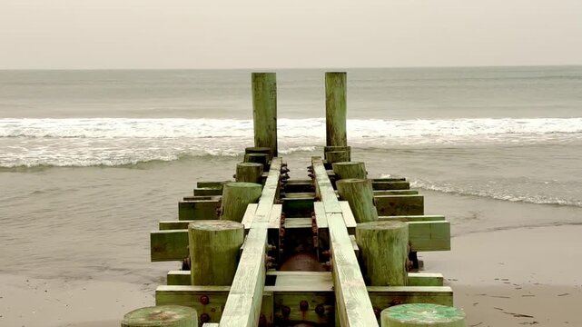 Wooden pier with pilings extending over beach out into the ocean 