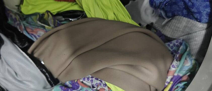 folds and textures of colorful clothing items, including beige, neon yellow, and patterned textiles, inside a domestic washing machine