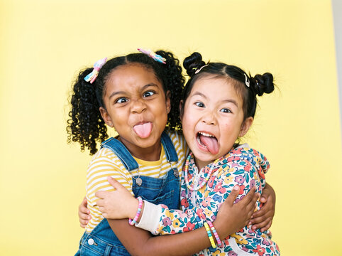 Two diverse young sisters hugging and making silly faces against a bright yellow studio background