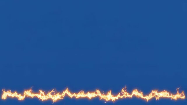 Continuous fire line with orange flames dancing against a clear blue sky during daytime