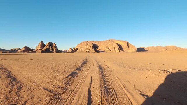 Driving in Wadi Rum at afternoon, car goes over sandy desert, sandstone sunlit mountains background distance, pov video