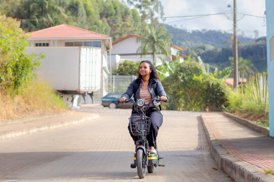 Young Black Brazilian woman commuting on an electric bicycle in a residential neighborhood, representing sustainable mobility, eco-friendly transportation, and modern daily urban life.