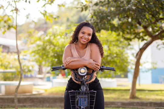 Young Black Brazilian woman enjoying a break with her electric bicycle, representing urban mobility, everyday commuting, and sustainable transportation.