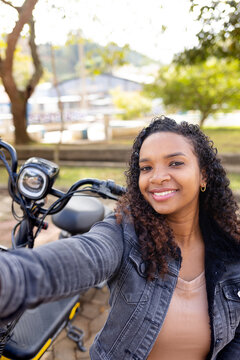 Young Black woman smiling and taking a selfie on her electric bicycle outdoors, representing sustainable urban mobility and youthful independence.