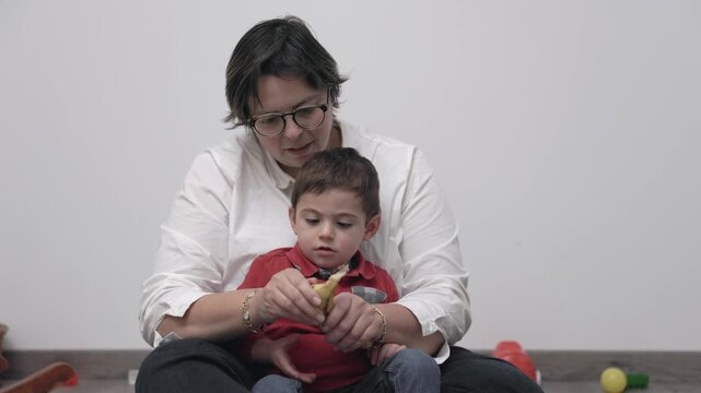 Mother teaching her toddler son how to peel a banana