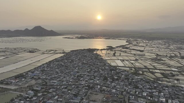 Aerial drone footage of sunset over Dam Nai Lagoon, Khanh Hoa, Vietnam, featuring golden reflections, tranquil waters, fishing boats and breathtaking coastal landscape at golden hour.
