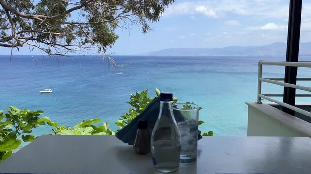 Water bottle and glass on restaurant table overlooking beautiful blue sea coast in Cyprus footage