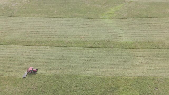 Aerial drone view of tractor working farmland with rows of hay bales