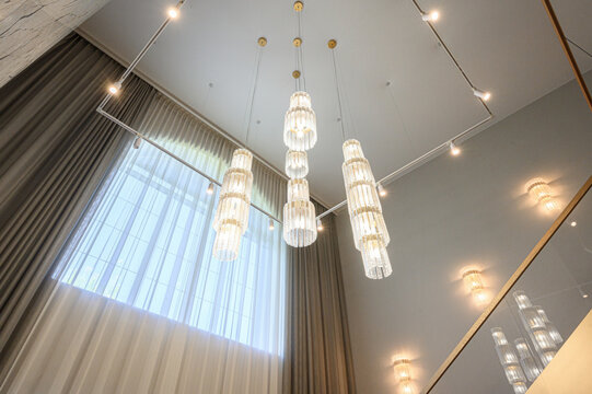 sophisticated interior spotlights tiered crystal chandeliers suspended from clean white ceiling. layered sheer and draped curtains frame tall window, complemented by sleek track lighting