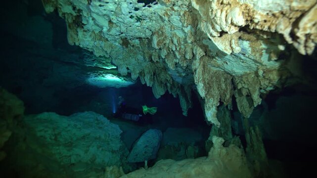 Professional cave diver swimming through an underwater cavern exploration in clear water.