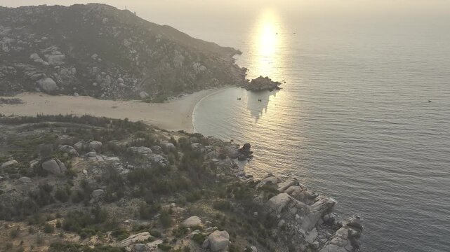 Aerial drone footage of sunrise over Mui Dinh Lighthouse and pristine beach in Khanh Hoa, Vietnam, showcasing golden morning light, dramatic coastline, turquoise sea and iconic coastal landmark.