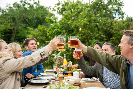 Group of people toasting with beer outdoors at a picnic table.