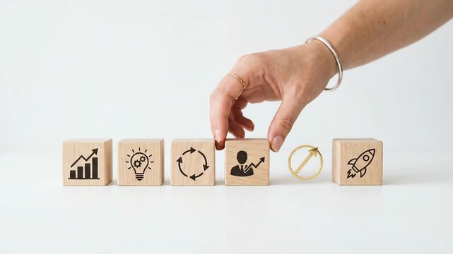 Woman hand placing wooden block with business icon on white table to demonstrate startup strategy and growth process