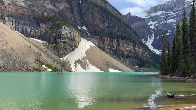 Beautiful view on the Moraine Lake in National Park of Banff, Canada. Two kayakers navigate a turquoise lake, framed by towering mountains and snow-capped peaks, with trees lining the shore.