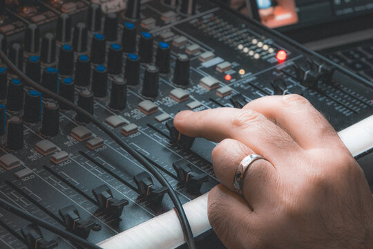 Close-up of a hand adjusting a knob on an audio mixing console in a studio, featuring a vintage warm cinematic color grading. Professional music production concept.