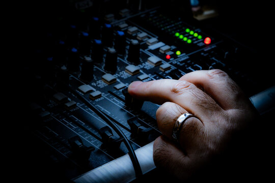 Close-up of a hand adjusting a knob on an audio mixing console in a dark studio. Professional sound engineer working on a music mixer board under dramatic lighting.