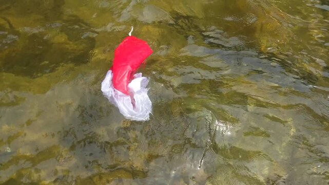 A red and white Santa Claus hat floating in the clear water of a river.
