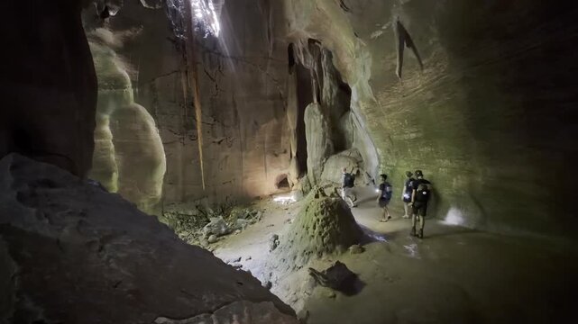 Small group of tourists walks through two chambers of Bukit Lawang Bat Cave, exploring the limestone cave beneath a colony of bats. North Sumatra, Indonesia. 