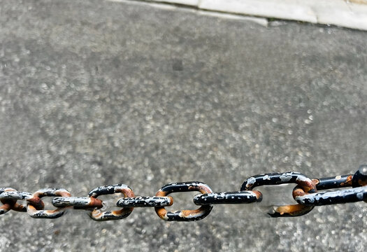 Rusty Black Iron Chain Across Asphalt Road