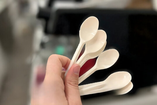 Hand Holding a Set of Small Ivory Plastic Spoons Indoors