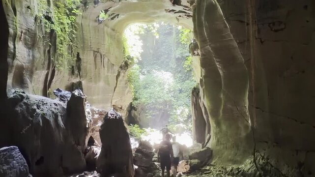 Bat Cave exit at Bukit Lawang as a small group of tourists walks away through the tropical forest after visiting the famous cave. North Sumatra, Indonesia.