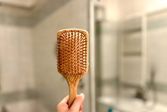 Hand Holding Wooden Paddle Hairbrush in Modern Bathroom