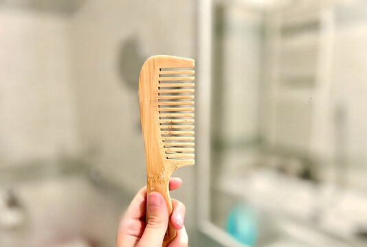 Hand Holding a Light Bamboo Hair Comb in a Modern Bathroom