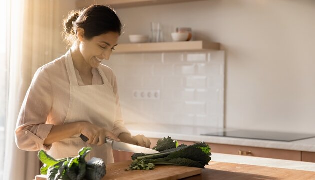 Woman cuts vegetables in a kitchen during sunlight hours while preparing a meal
