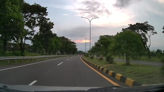 Front Dashcam Driving Along Tree-Lined Curved Road Under Dramatic Cloudy Afternoon Sky in Sidoarjo East Java Indonesia
