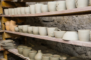 Clay pottery displayed on shelves in a workshop, showing various shapes and sizes before being...