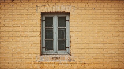 Fototapeta premium Brick wall with a small, old window with blue wooden shutters.