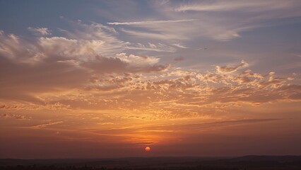 Fototapeta premium Sunset sky with clouds and a setting sun on the horizon. Nature and sky scene. Beautiful evening landscape with warm colors.