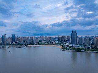 Naklejka premium Zhanjiang Jinshawan riverside city skyline at dusk with modern high-rises and calm water