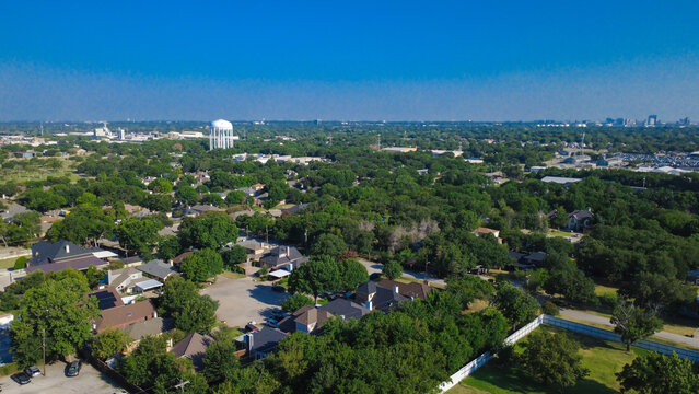 Densely packed green tree canopies shelter single family homes and neighborhood pathways. Secluded residential blocks feature expansive foliage wrapping around local properties, Irving, TX