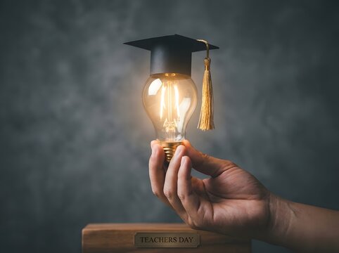 Hand holding a glowing light bulb with graduation cap for celebration of teachers day event