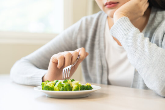 Diet in bored concept, Ketogenic, Low carb, Intermittent Fasting young woman dieting holding fork at broccoli on salad plate tired with eat fresh vegetables. Nutrition clean, healthy food good taste.