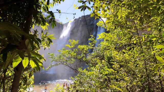 Salto Corumba waterfall naturally framed by green foliage with tourists enjoying the pool on a sunny day
