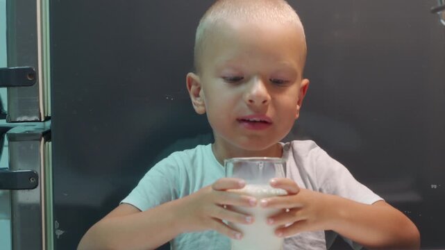 A happy little boy holds a fresh glass of milk in a cozy kitchen. He looks down at his delicious drink with joyful anticipation and quiet satisfaction.