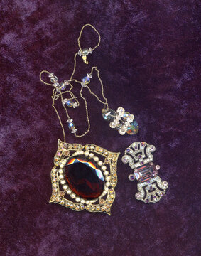 Vintage small jewelry a bit kitch, brooches and neklace on purple velvet background
