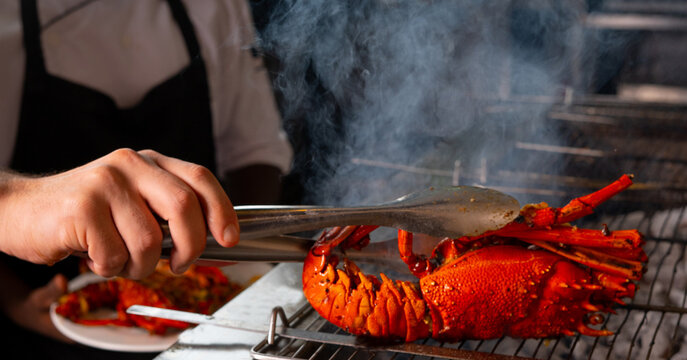 Professional chef preparing and grilling premium red lobster on a charcoal BBQ grill
