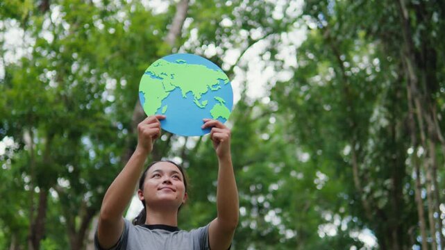 Young woman holding an earth globe in a green forest. Concept of earth care, environmental protection, saving the planet, sustainability, and eco-friendliness.