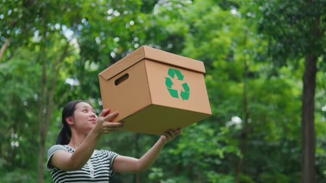 Young Asian woman volunteer holding a recycling box in the park. Concept of recycling, environmental protection, sustainability, zero waste, and ESG strategy on green natural forest background.