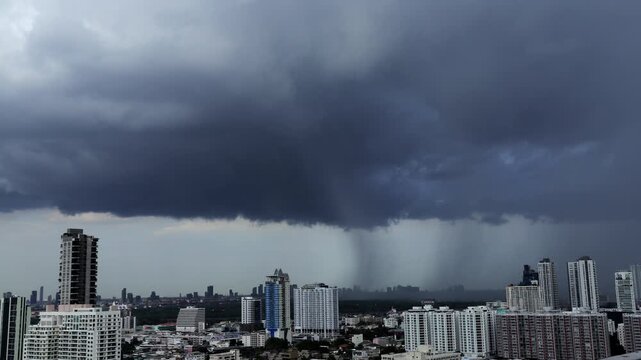 Time-lapse of a dramatic rain shaft descending from dark storm clouds over a modern city skyline.