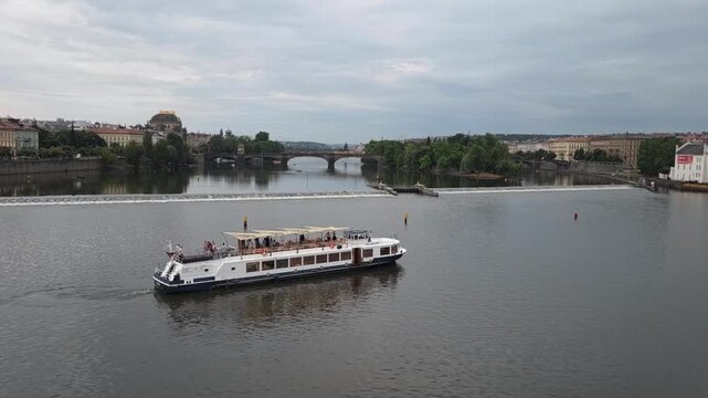 Tracking shot of tour boat cruising along river past bridge and waterfront in city on overcast daytimeю Riverboat on the Vltava in Prague