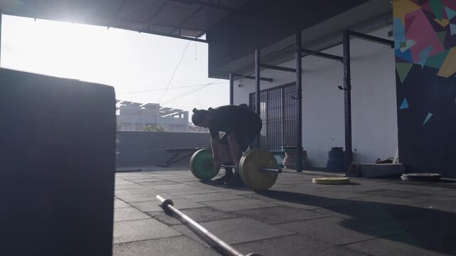 Bearded South Asian male athlete performing a conventional barbell deadlift during a strength training workout in a modern indoor fitness studio. Collection: WORKOUTSERIES2026