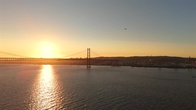 An extended drone panorama sweeps across the full breadth of the Tagus River bathed in warm amber evening light.
